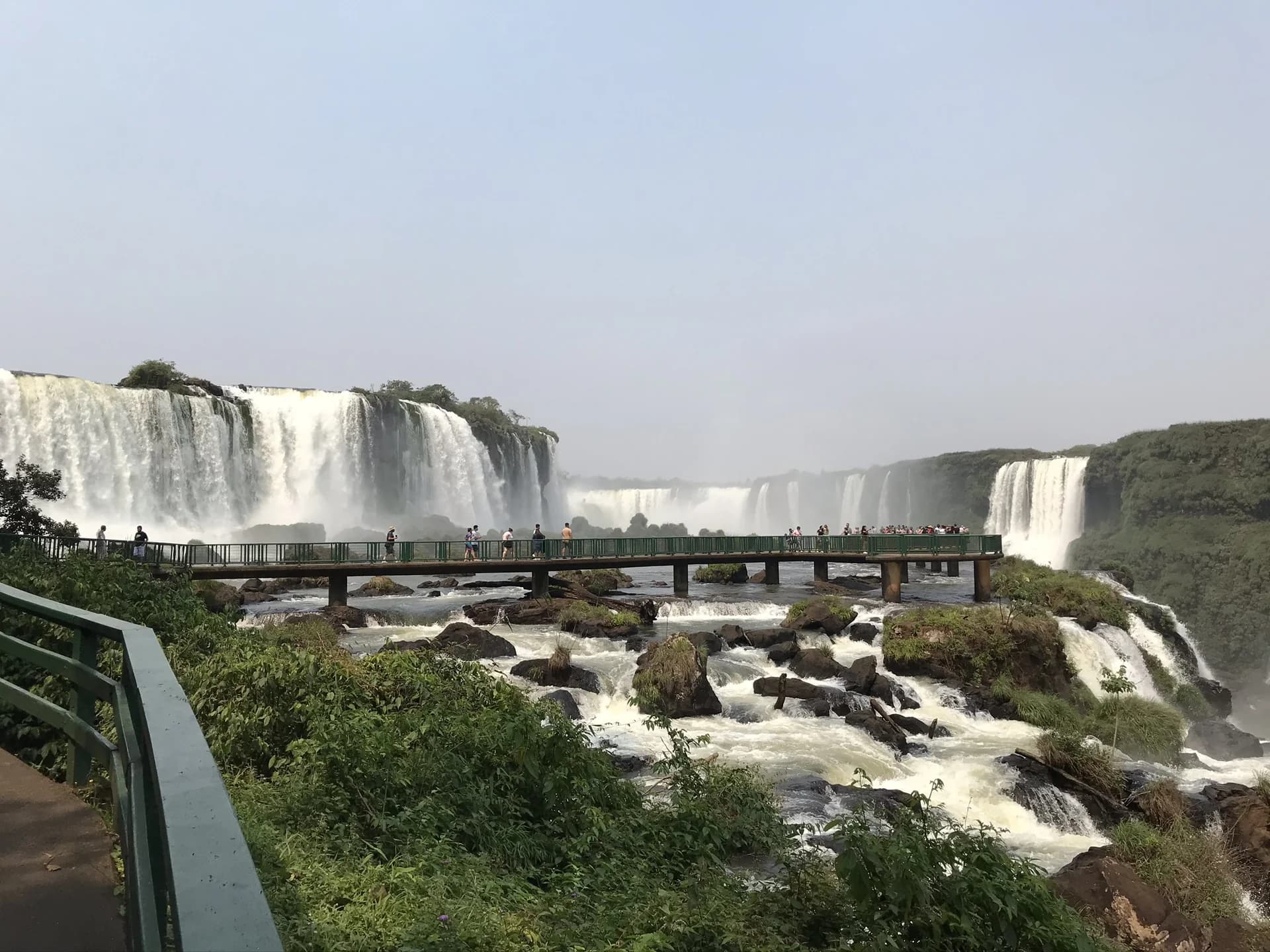 Visitors on the elevated walkway over the Iguazu River on the Brazilian side of Iguazu Falls, with the panoramic wall of Argentine falls behind